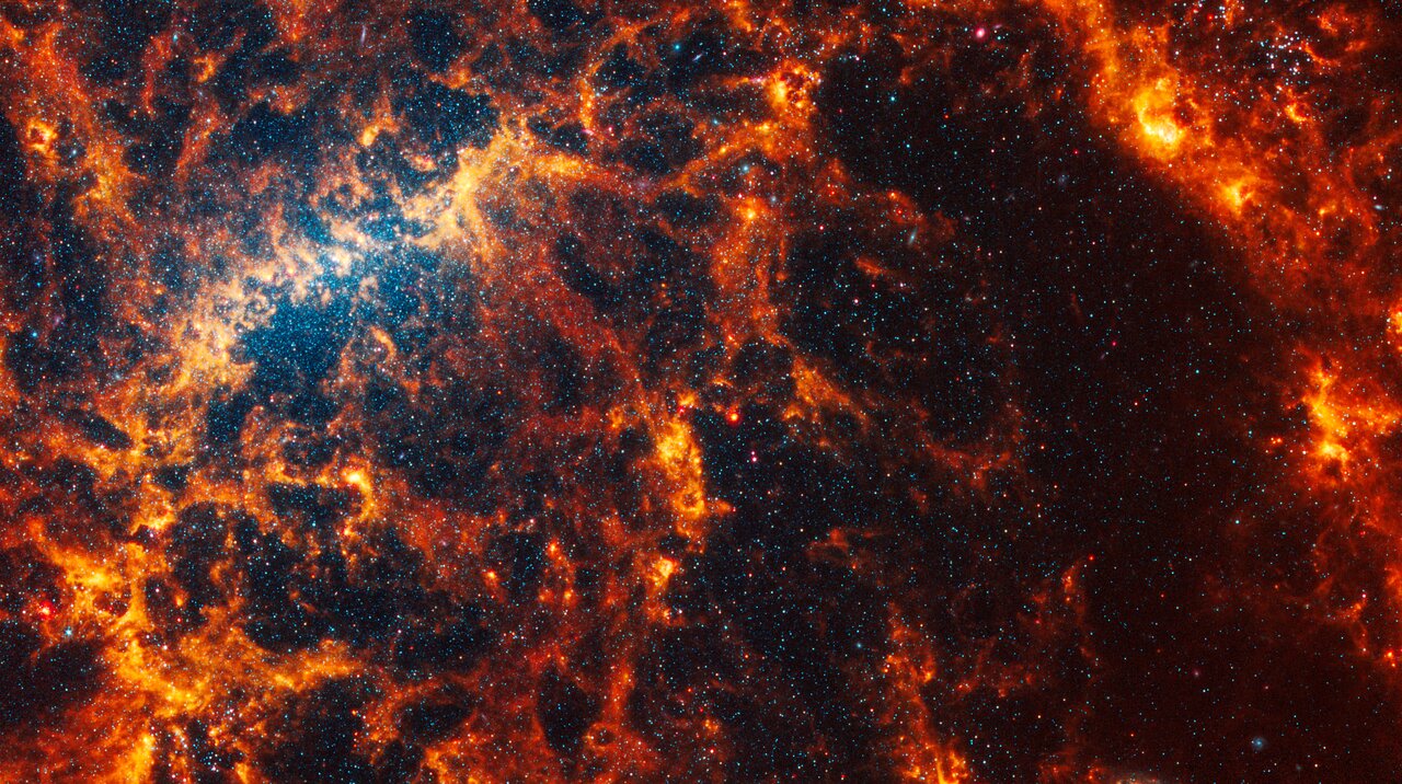 Webb’s image of NGC 5068 shows a portion of a messy face-on barred spiral galaxy in shades of white, yellow, orange, and red. The galaxy’s bar is a bright yellow arc-shaped region toward the centre-left, and it is very difficult to see a spiral shape.