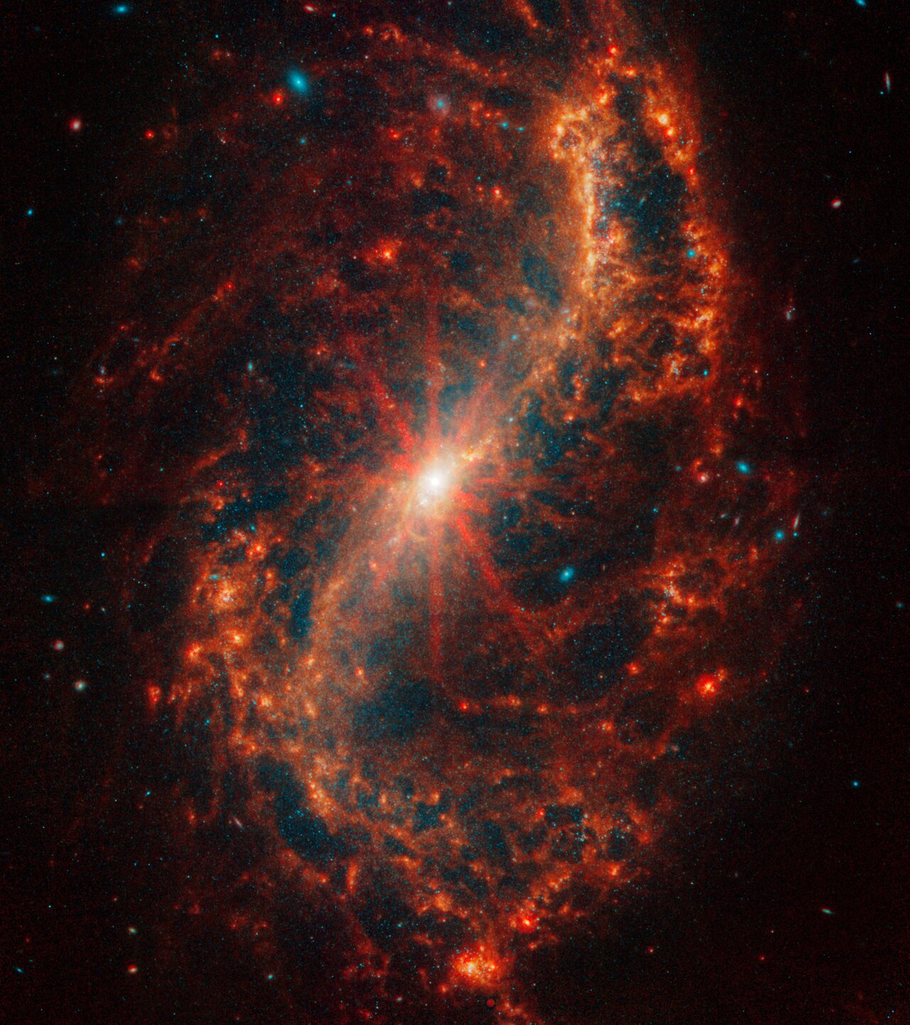 The central core of Webb’s image of the galaxy NGC 7496 begins as a bright white dot that melts into bright oranges. Eight prominent diffraction spikes emanate from the centre. A bright orange arc that looks like a thin, backward S forms the bar and two of the face-on spiral galaxy’s arms.
