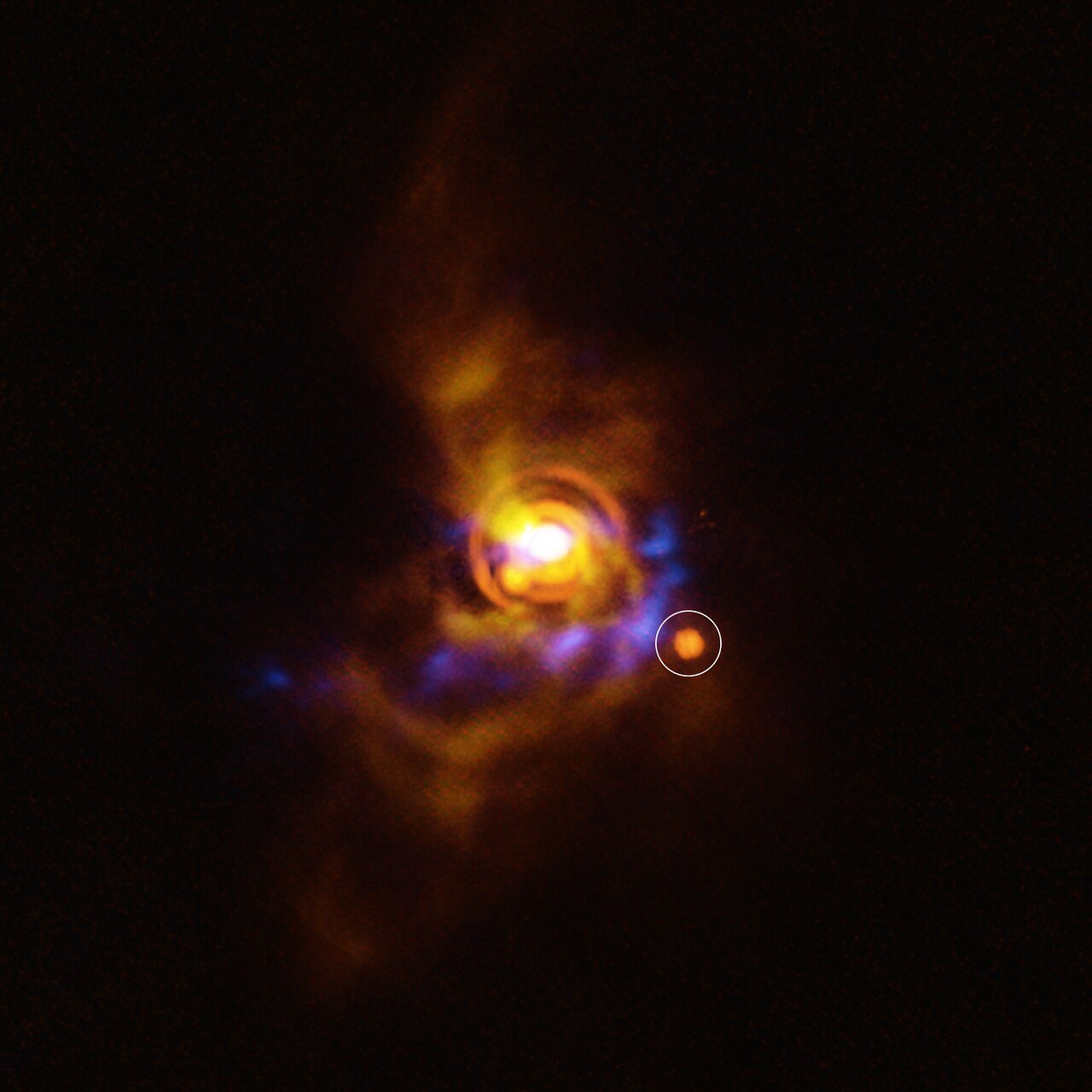 This image shows a possible companion orbiting the young star V960 Mon. The star, located more than 5000 light-years away, is surrounded by a disc with intricate features. Previous analysis of the disc showed that it contains clumps of unstable material that could collapse to form a companion object. The new candidate found here could be either a planet or a brown dwarf –– an object bigger than a planet that didn’t gain enough mass to shine as a star. The candidate object was found with ESO’s Very Large Telescope (VLT), using its new Enhanced Resolution Imager and Spectrograph (ERIS). The new ERIS data are shown here in orange, overlaid on older images of the dusty disc as seen with the VLT’s SPHERE instrument (yellow) and the Atacama Large Millimeter/submillimeter Array (ALMA, in blue). Credit: ESO/A. Dasgupta/ALMA (ESO/NAOJ/NRAO)/Weber et al.