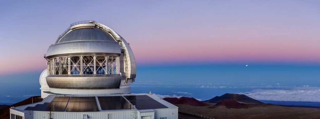 Breathtaking views of astronomical events are a never-ending source of great excitement for the staff at Gemini North, one half of the International Gemini Observatory, supported in part by the U.S. National Science Foundation and operated by NSF NOIRLab. One such example is the lunar eclipse taking place in the distance on the right side of this image, captured in 2019. It is seemingly encased in the dark blue band above the horizon. Lunar eclipses occur when Earth moves between the Sun and the Moon. The Moon, which is only visible by the sunlight reflected off it, is darkened by the Earth’s shadow. An eclipse like this one can be viewed from anywhere on Earth where the Moon is visible, though the extent of the eclipse depends on how aligned the Moon is to Earth’s shadow and one’s viewing location. In 2022, for example, the two lunar eclipses, both total eclipses, were visible from Gemini North in Hawai‘i.Credit: International Gemini Observatory/NOIRLab/NSF/AURA/J. Chu