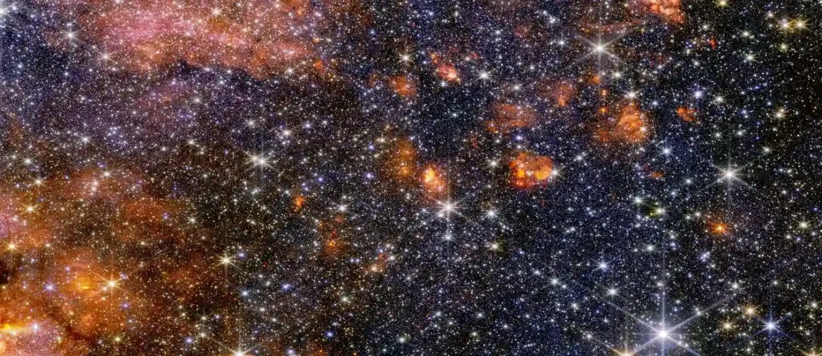 Sagittarius B2 (Sgr B2) molecular cloud A wide view of a region of space filled with stars and clumps of orange clouds.